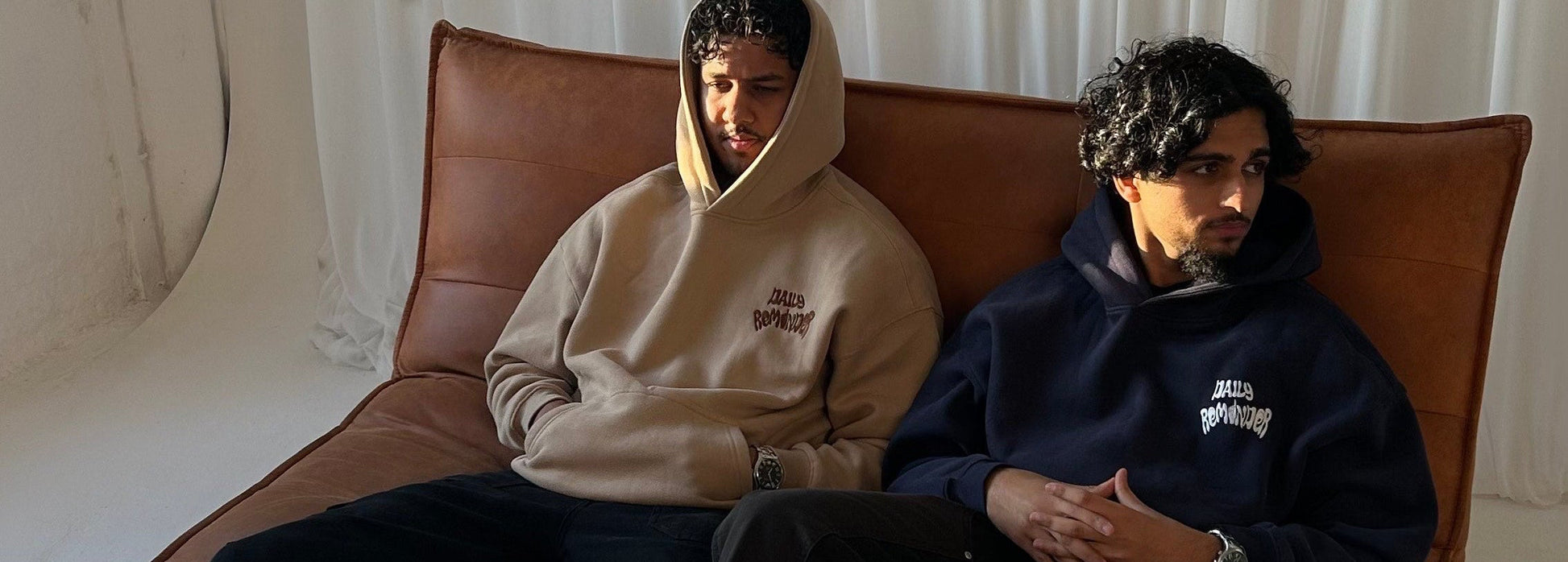 Two people sitting on a brown sofa against a white curtain background